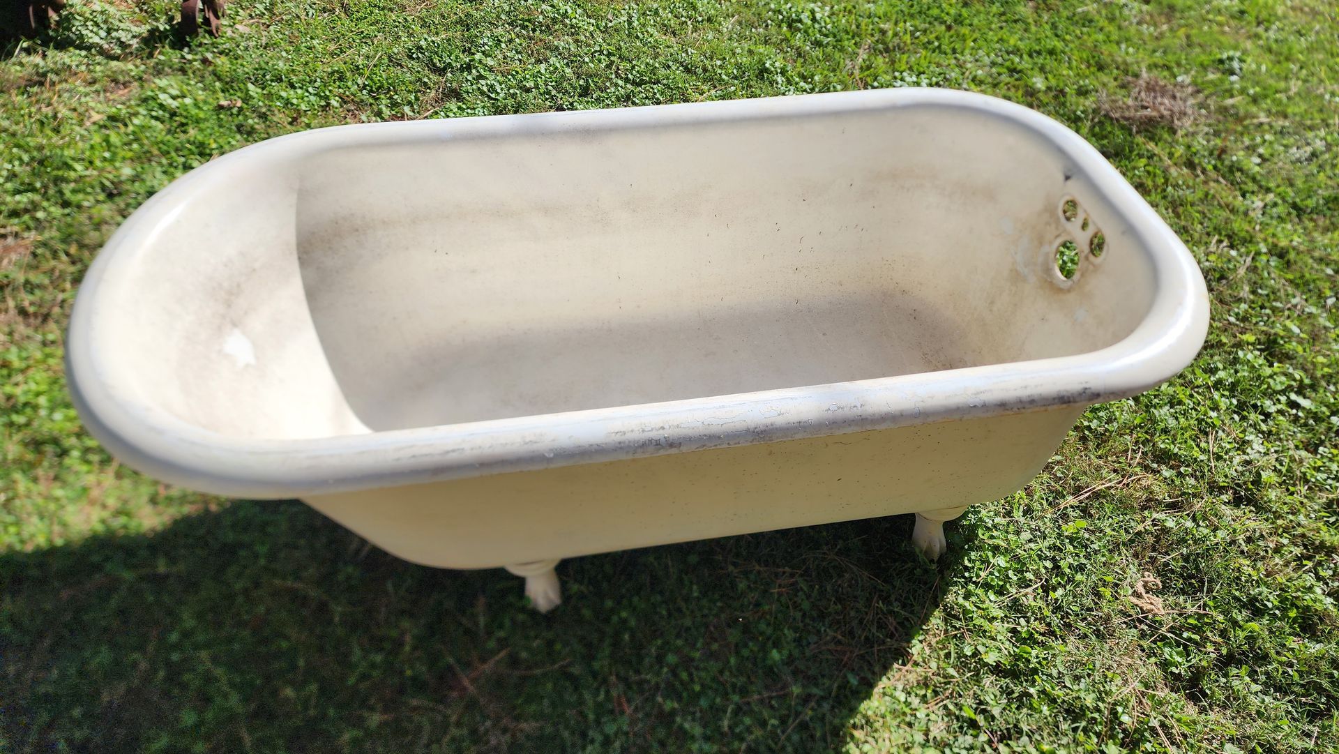 Old cream-colored clawfoot bathtub sitting on grass outdoors.