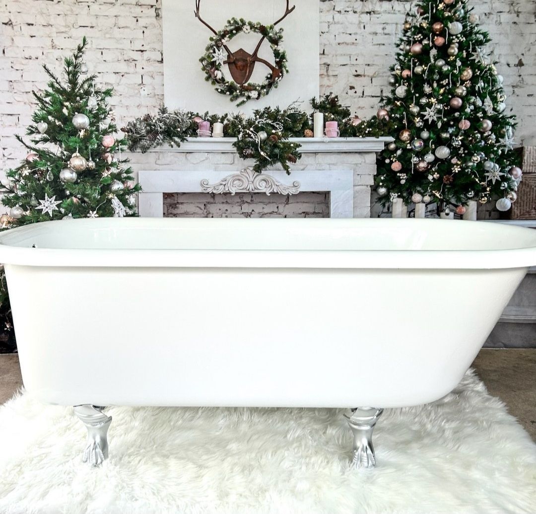 White clawfoot bathtub in a festive room with Christmas trees, garland, and a wreath on the mantel.