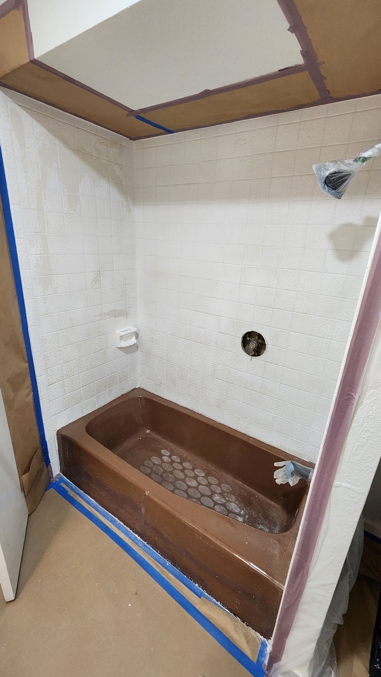 Small unfinished shower stall with a wood base, white walls, and blue tape along the floor edges.