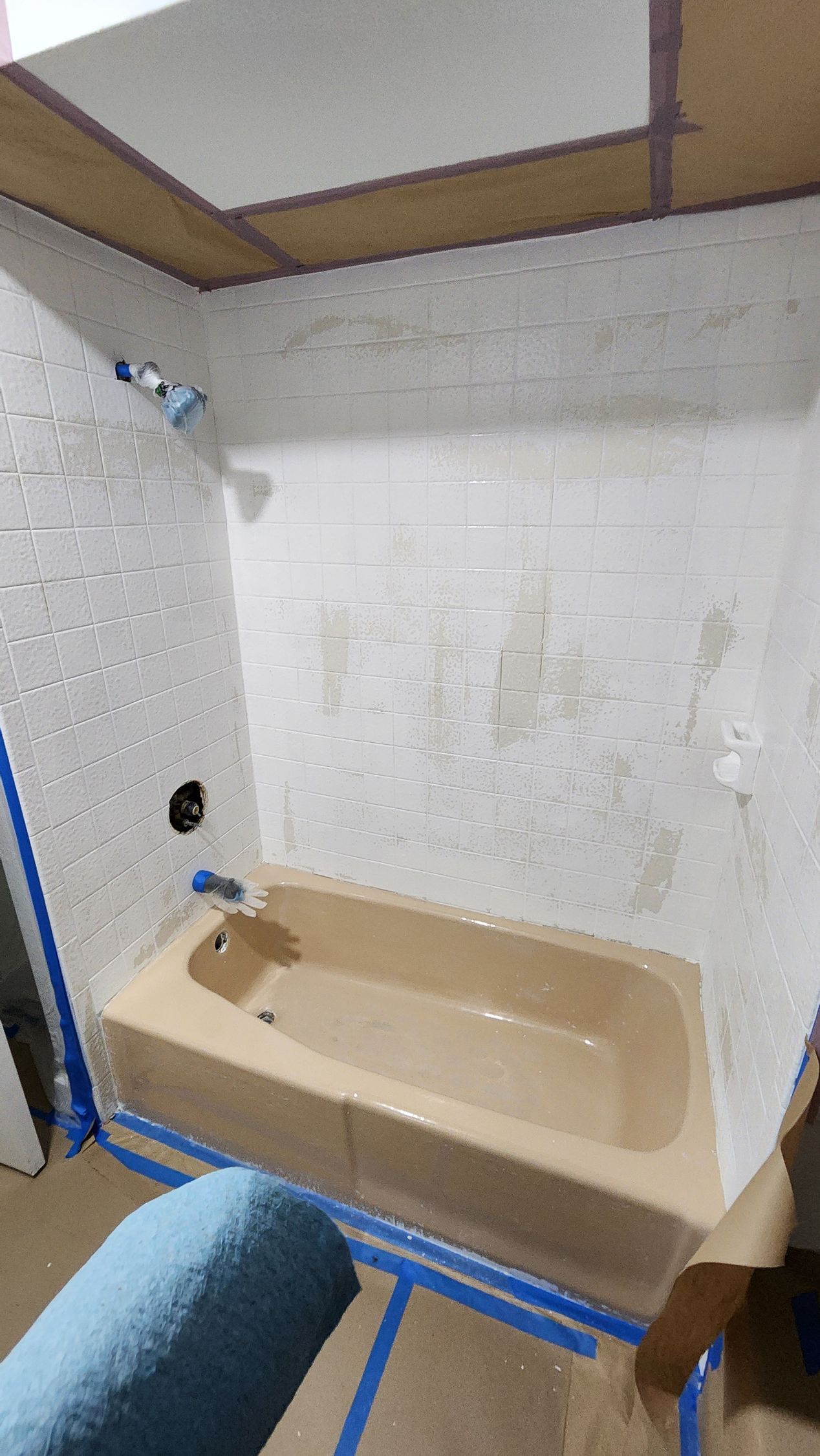 Small beige bathtub in a bathroom alcove, with blue tape marking the floor and wall edges.
