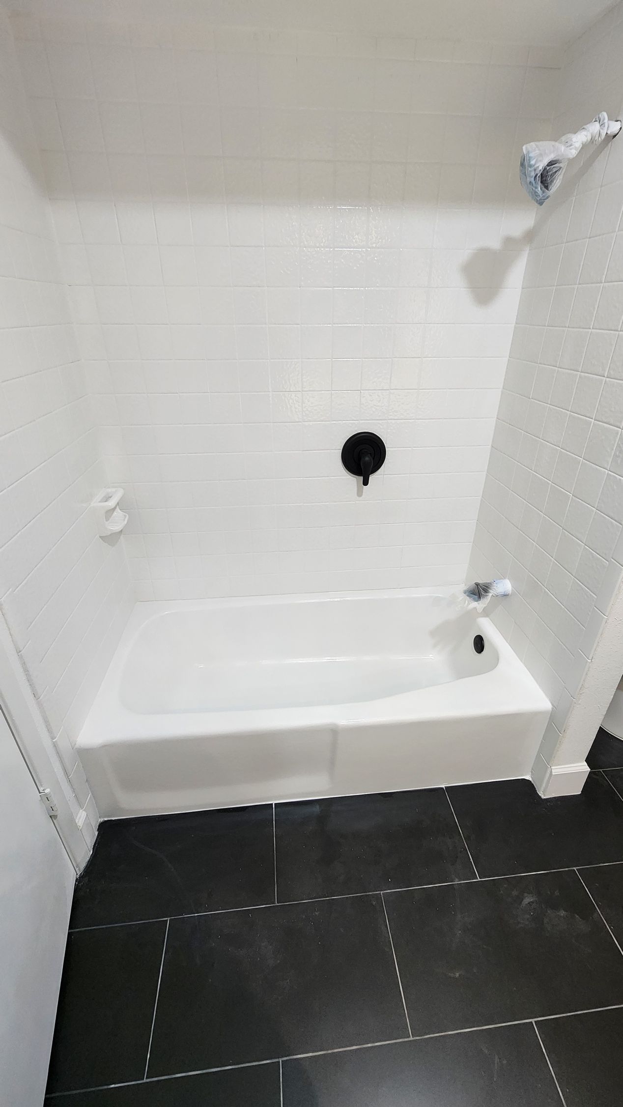 Small white tiled shower alcove with built-in tub and dark floor tiles
