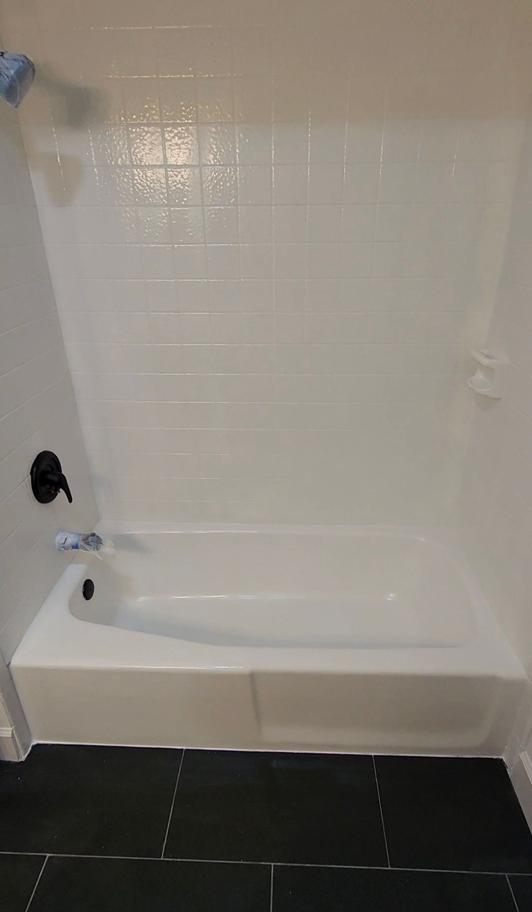 White-tiled bathtub alcove with shower wall, black floor tile, and chrome faucet fixtures