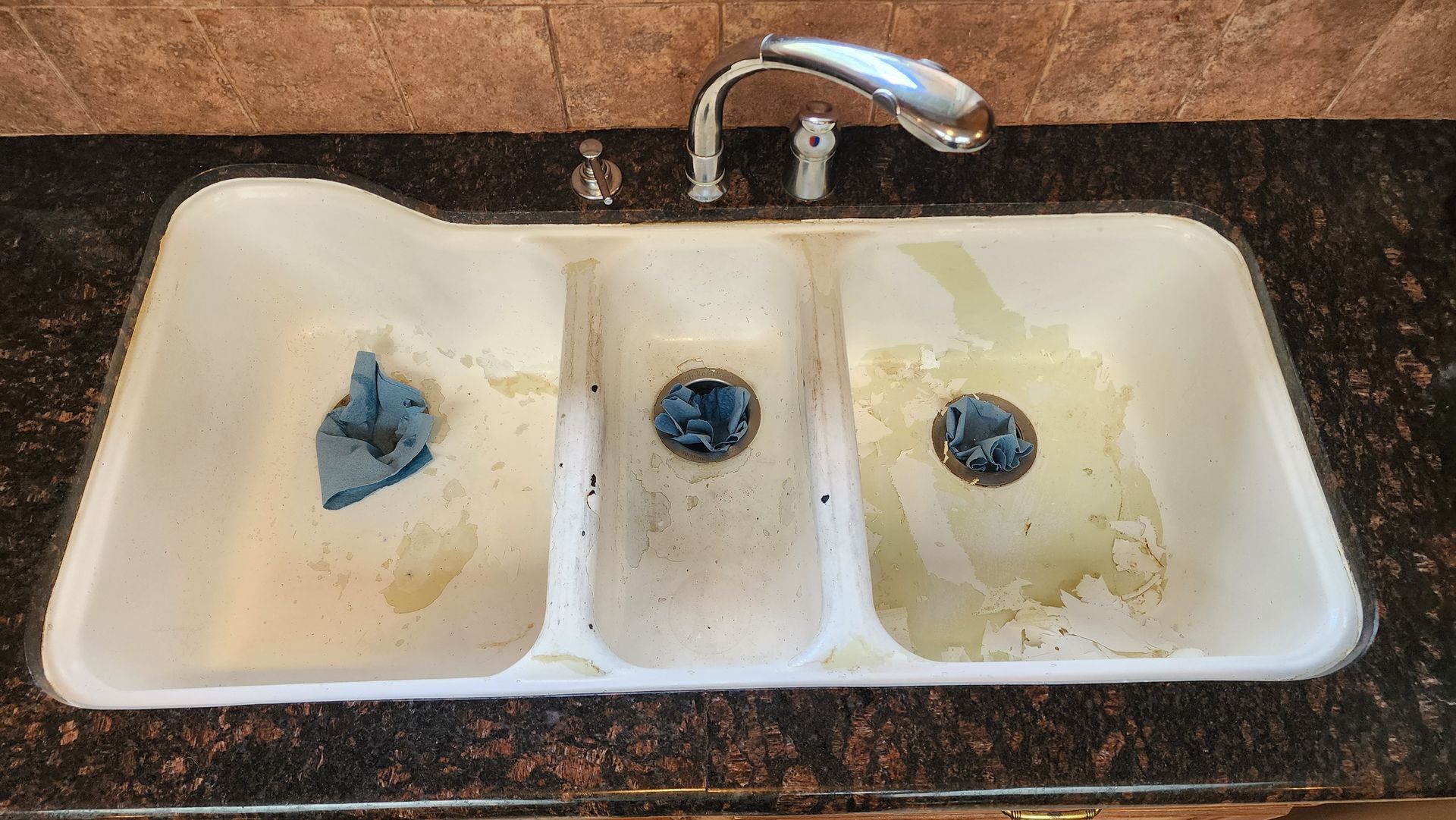 Dirty white bathroom sink with three basins, a faucet, and a blue object in the left basin.