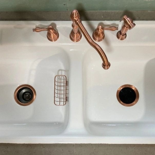 White double kitchen sink with copper faucet, left drain strainer, and right drain opening