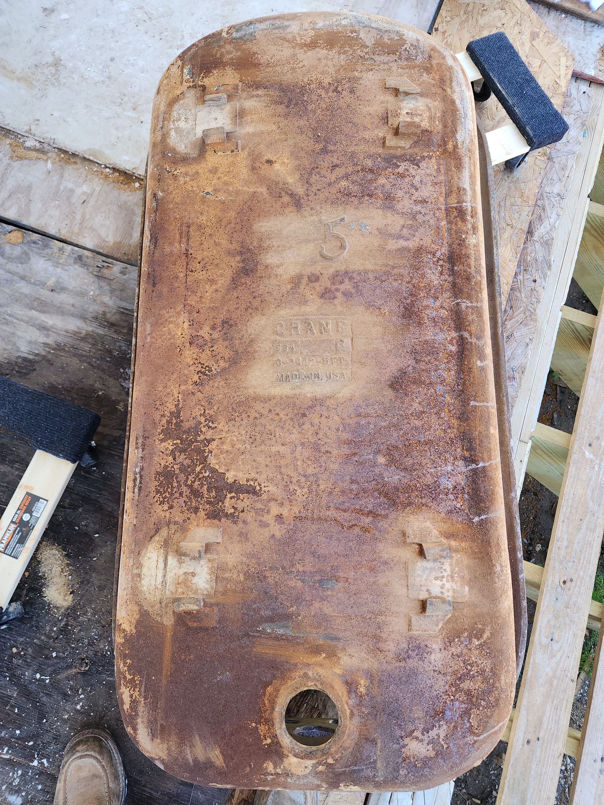 Rusty metal tank lying on a wooden surface, with a round hole near the bottom.