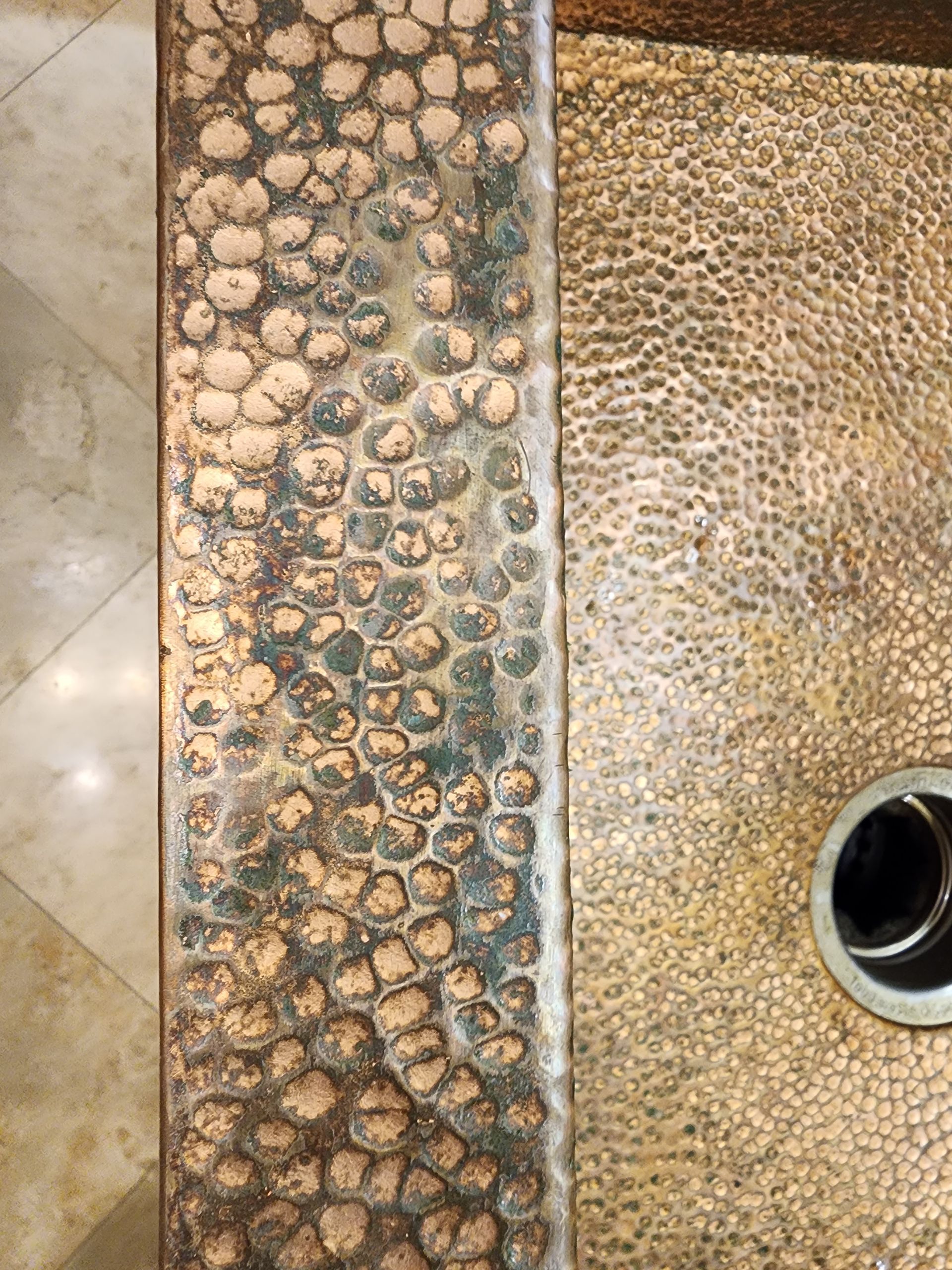 Textured beige and blue pebble mosaic beside a speckled surface with a round drain opening