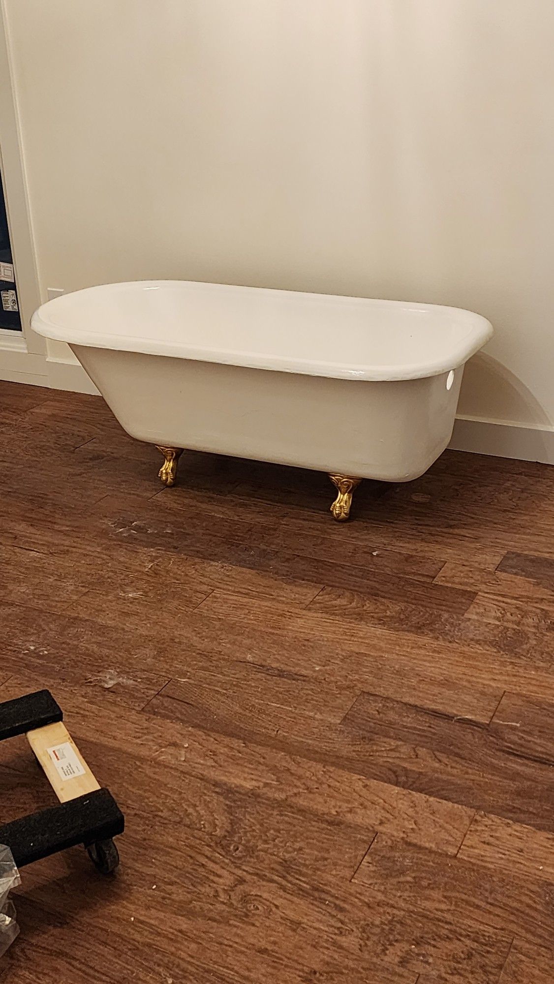 White freestanding bathtub on small gold wheels against a beige wall over a wood floor