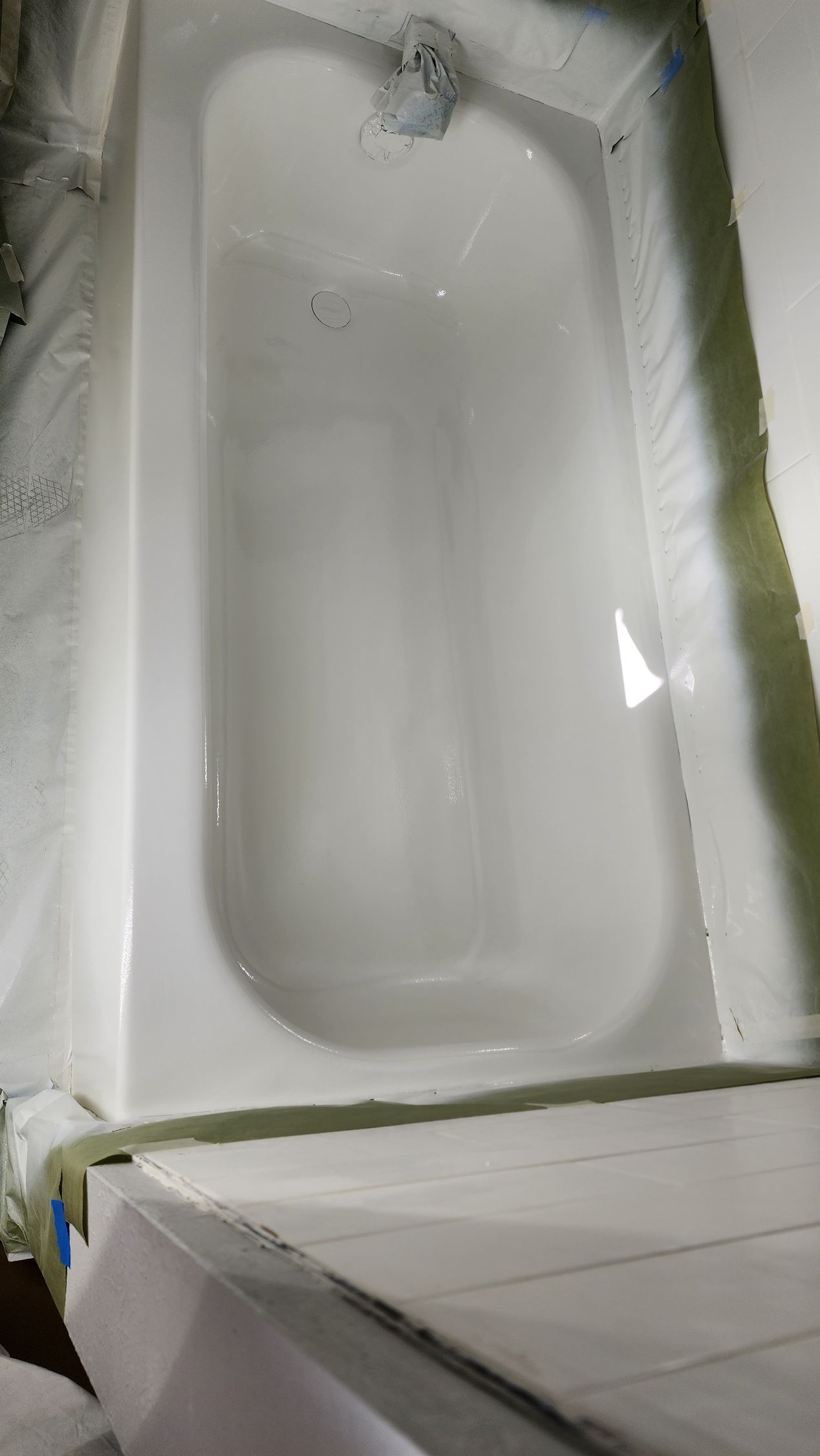 White bathtub in a tiled bathroom, viewed from above, with a chrome faucet at the top end.