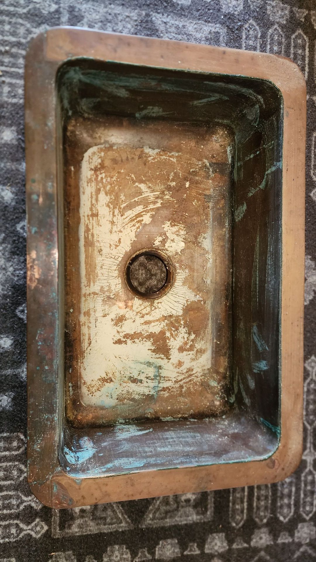 Rusty old rectangular sink basin with a drain hole, viewed from above on a patterned surface