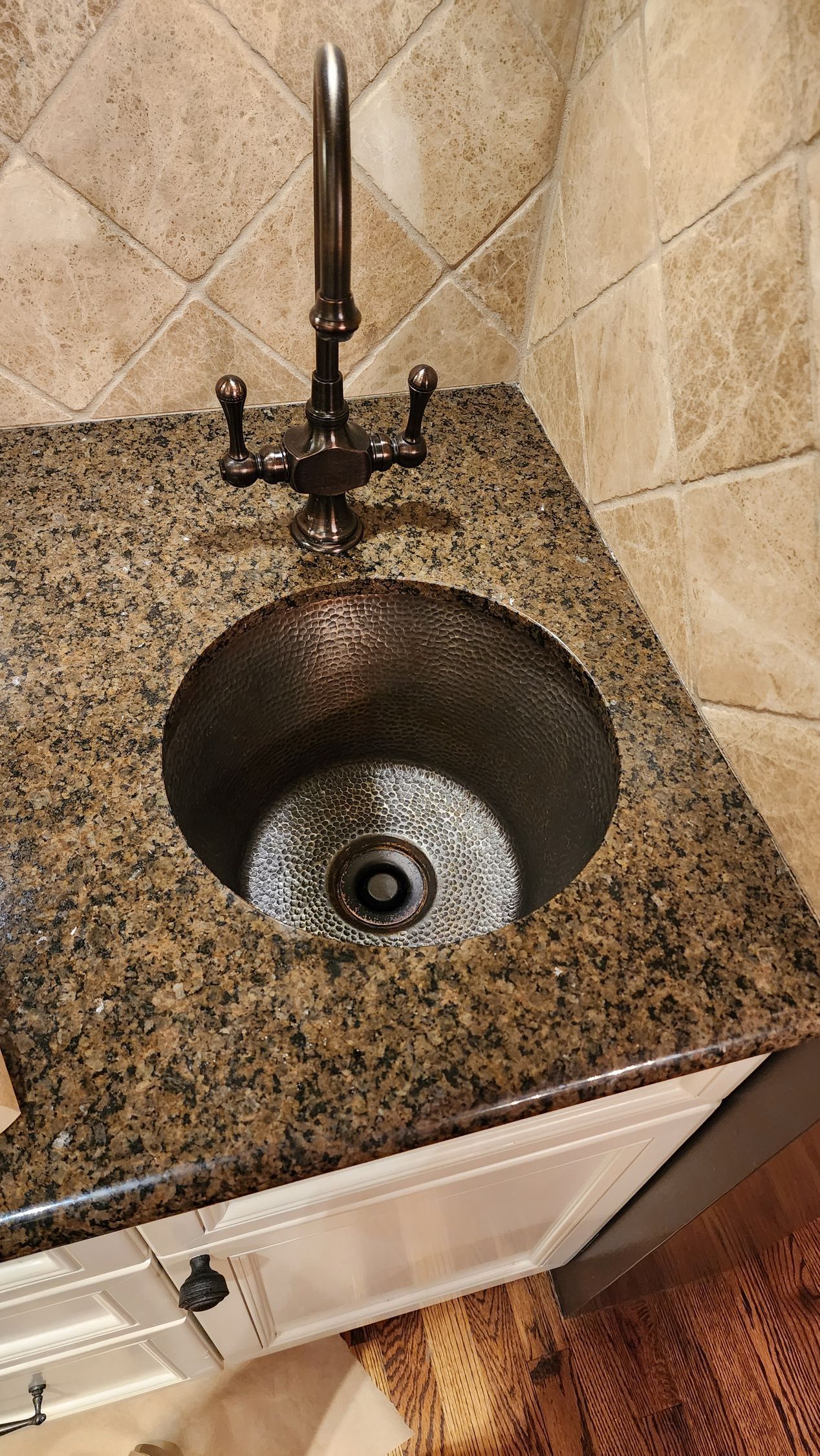 Granite bathroom countertop with an undermount sink and chrome faucet against beige tiled wall