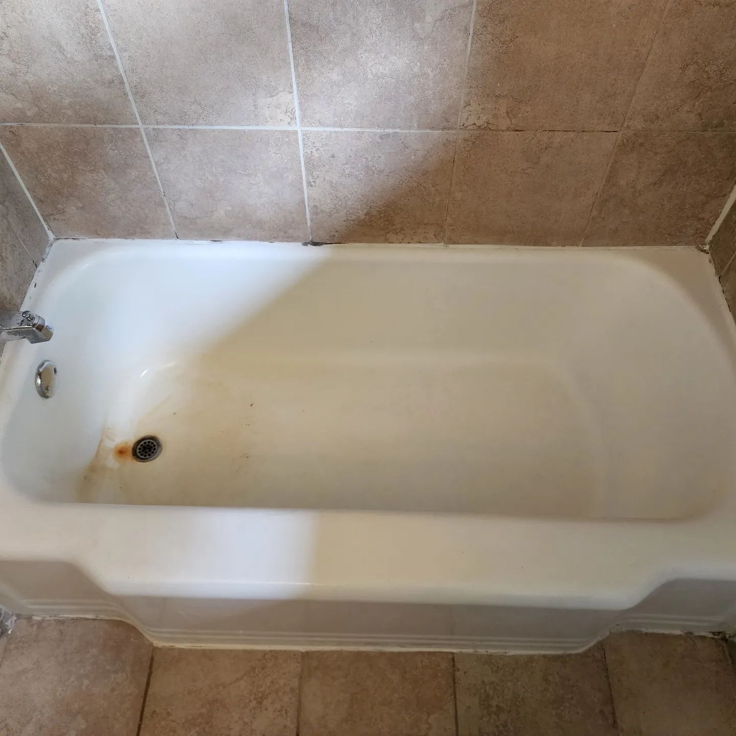 White bathtub with a drain and faucet against beige tiled walls