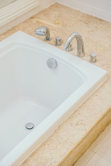 Bathtub with chrome faucet and controls on beige tiled bathroom surround