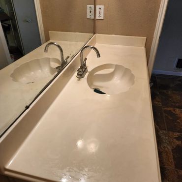 Bathroom vanity with two sinks, one faucet, and a large mirror on a beige countertop
