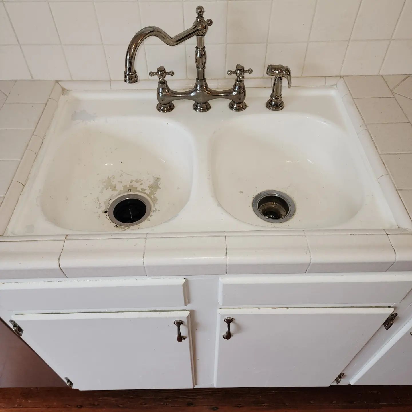 Double kitchen sink with dirty basins and an old chrome faucet on a tiled countertop