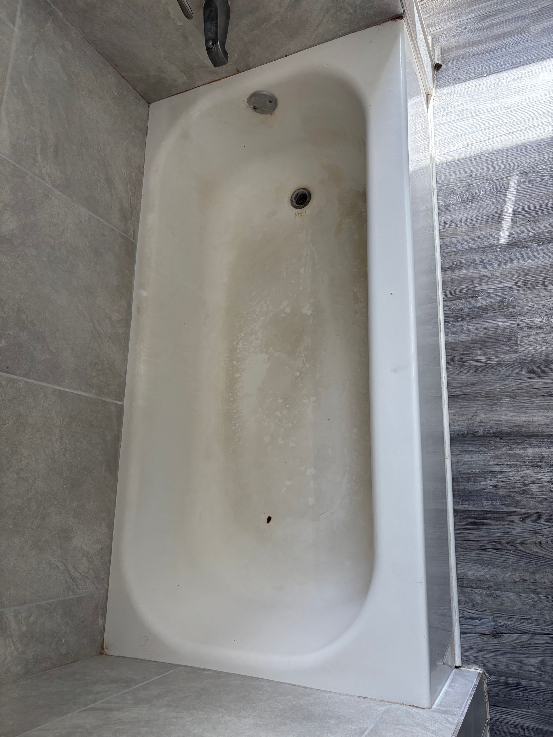 White bathtub with tiled surround and showerhead, viewed from above.