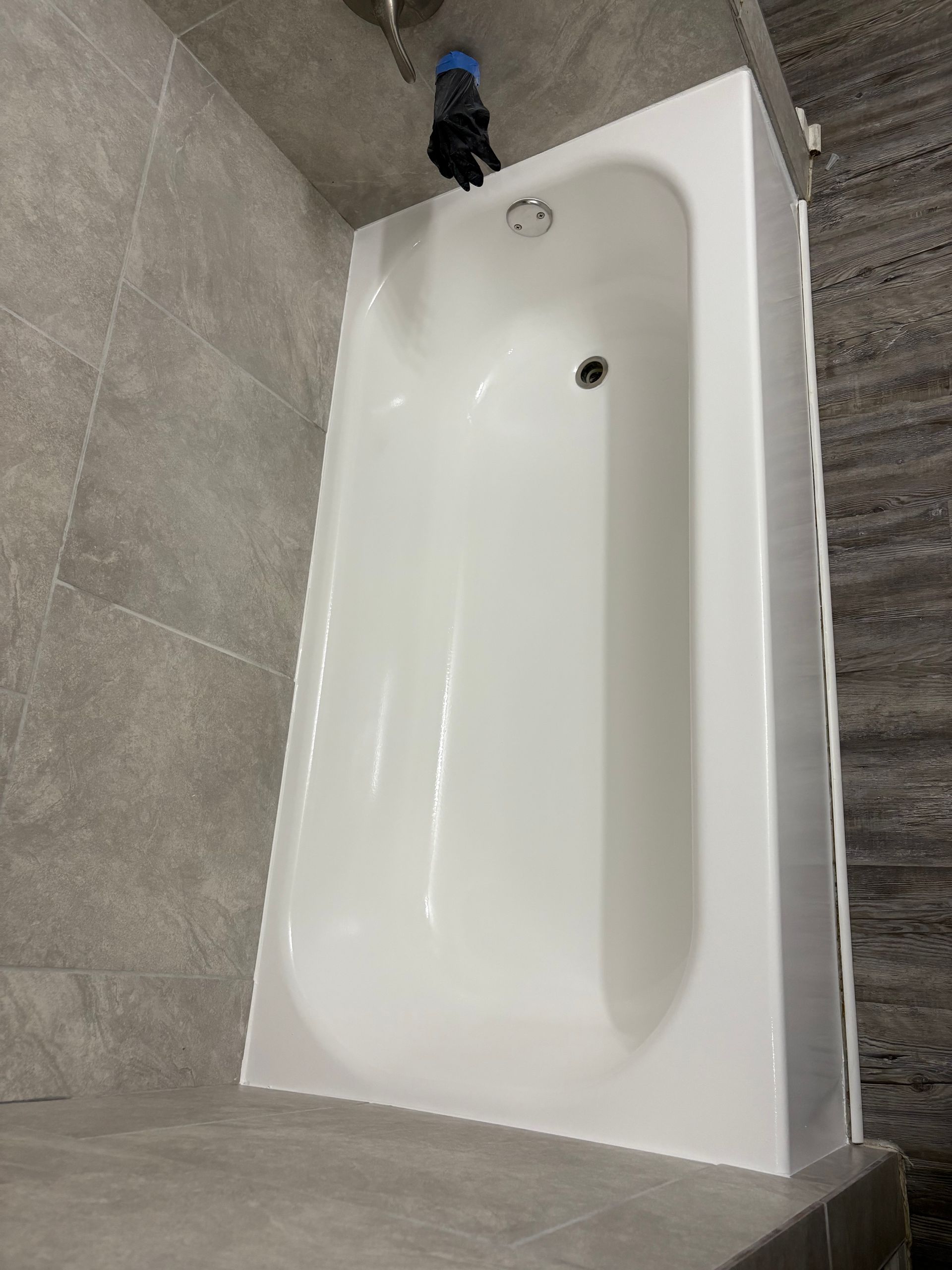 Empty white bathtub in a gray-tiled bathroom, viewed from above.