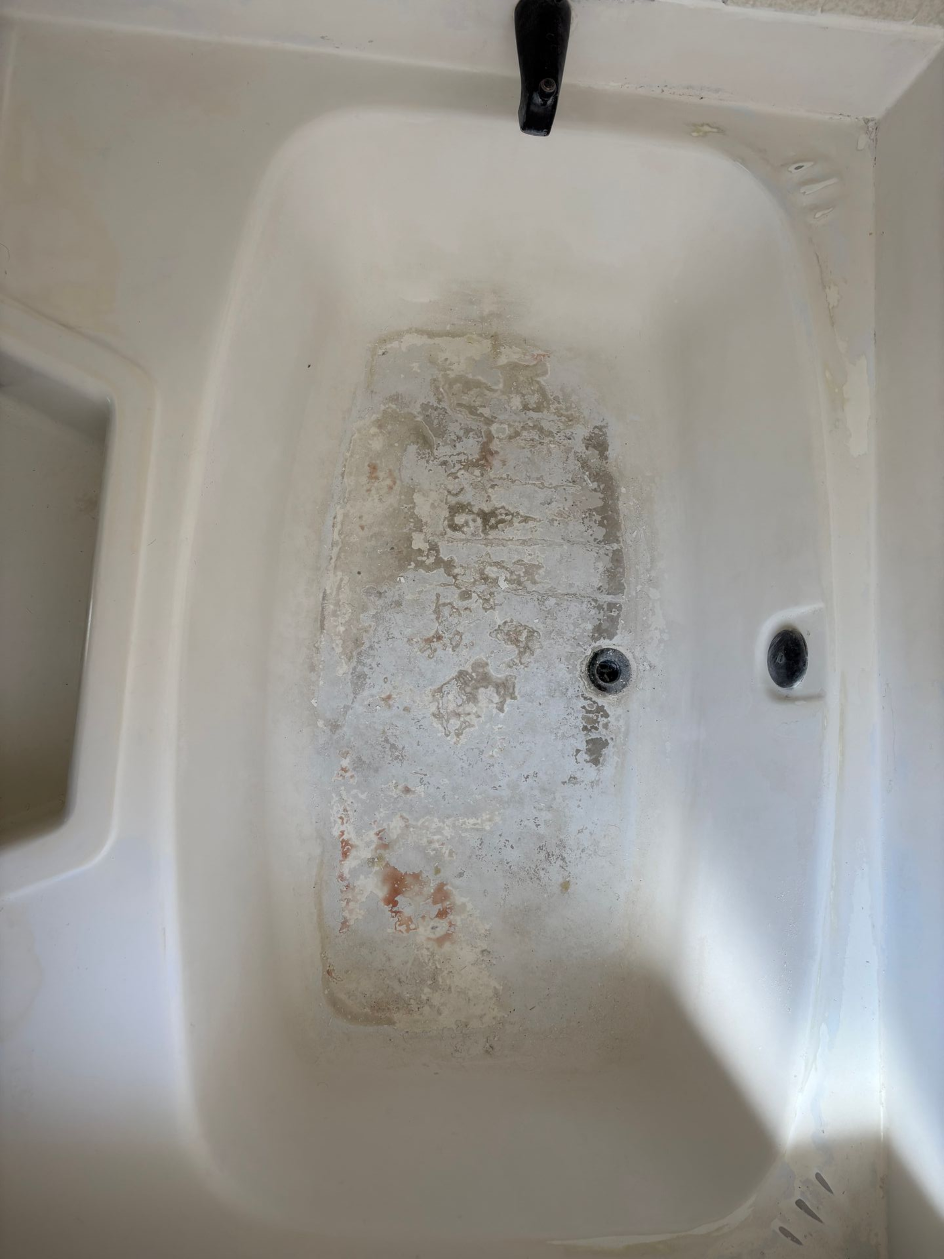 Dirty white bathtub with peeling stains and a drain hole on the right side