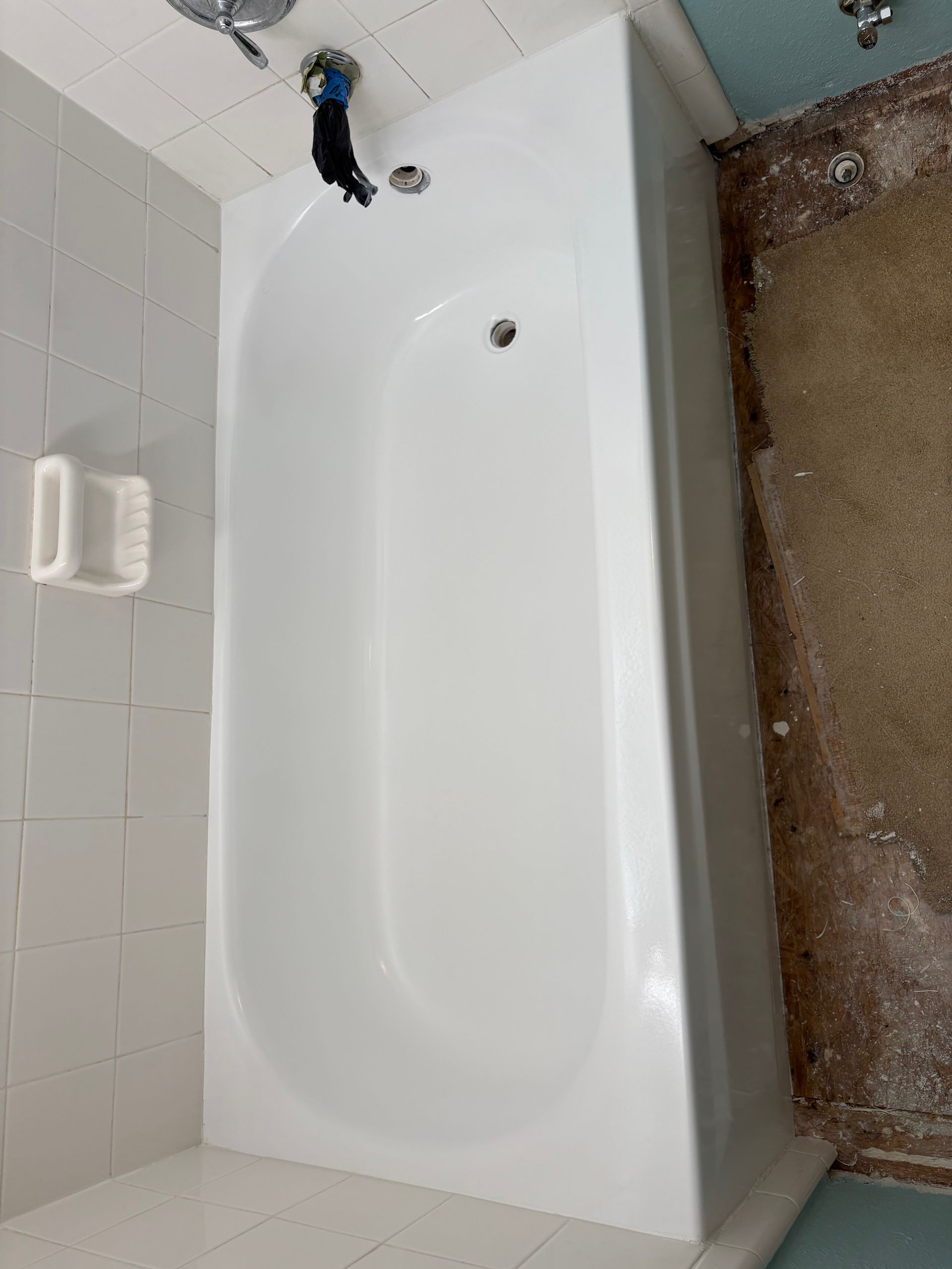 White bathtub in a bathroom beside a tiled shower wall and beige carpeted floor.