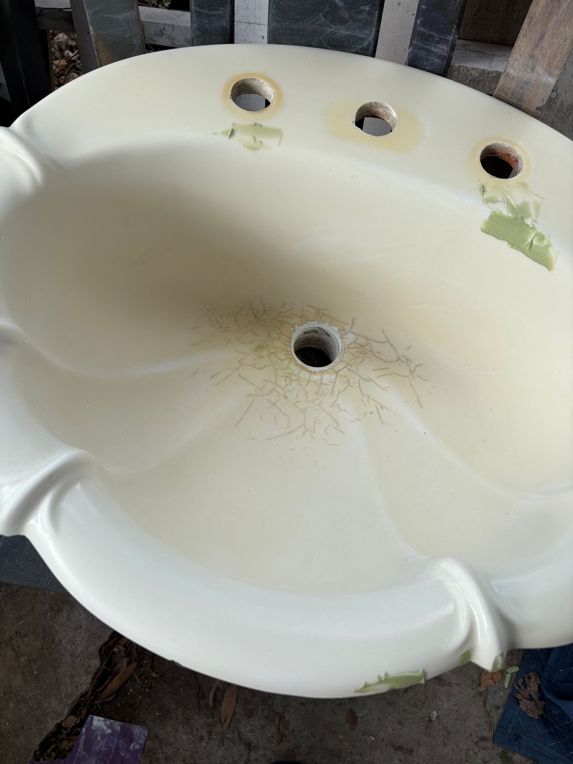 Cracked white porcelain sink basin with drain hole, holes at the back, and visible stains and wear