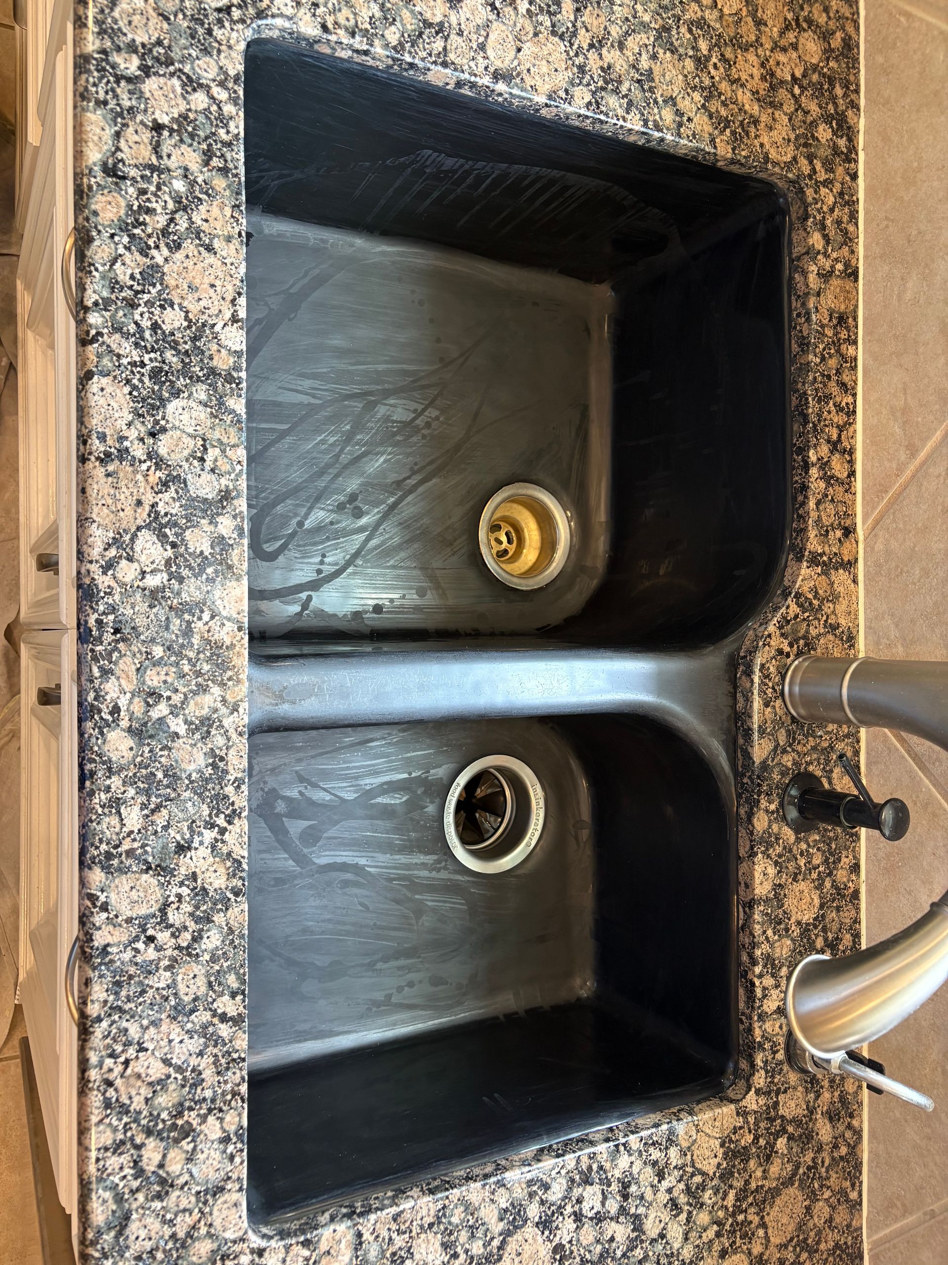 Double kitchen sink with granite countertop and chrome faucet, one drain showing a gold strainer.