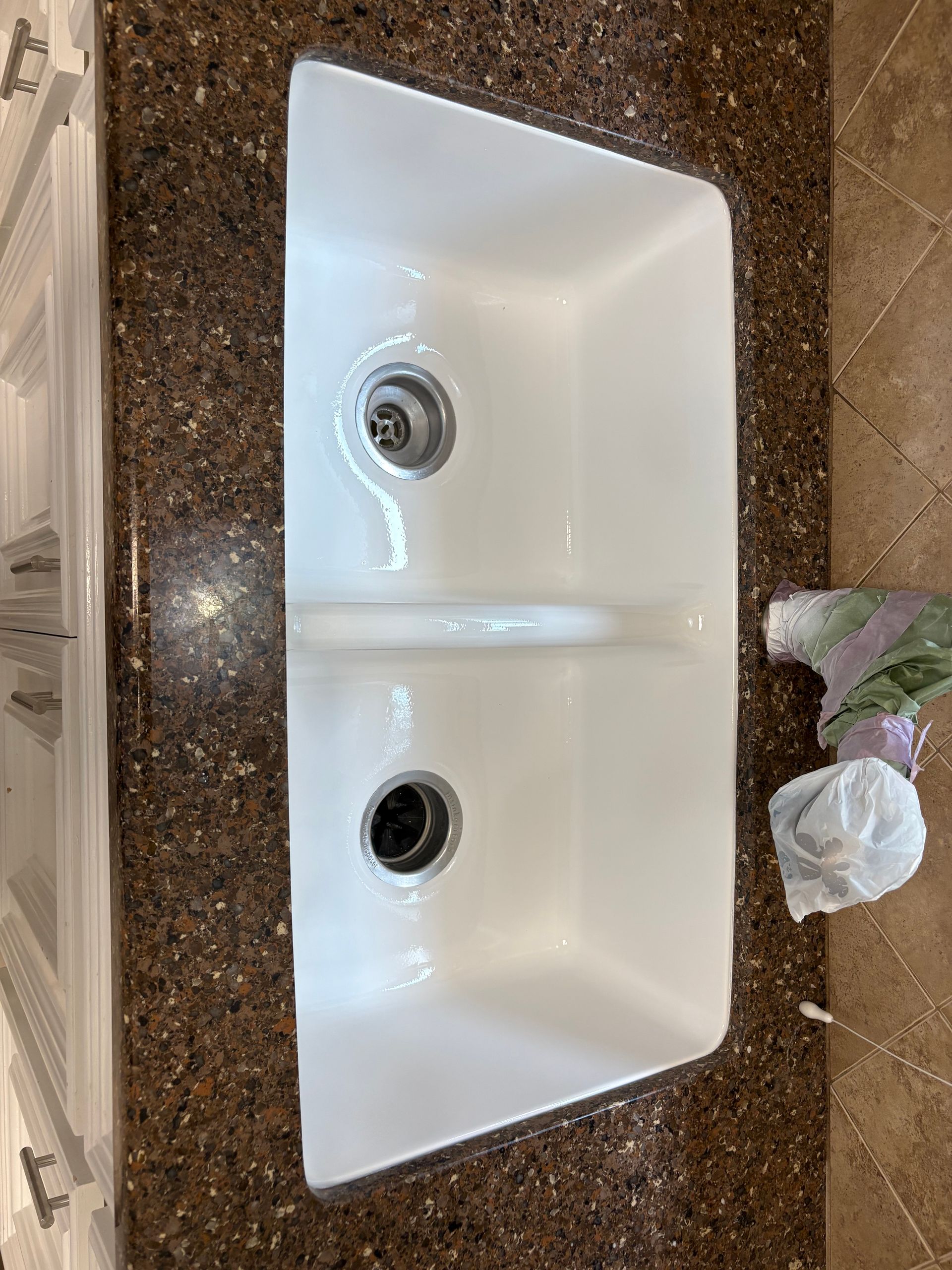 Double-basin white sink with brown speckled countertop and drain openings