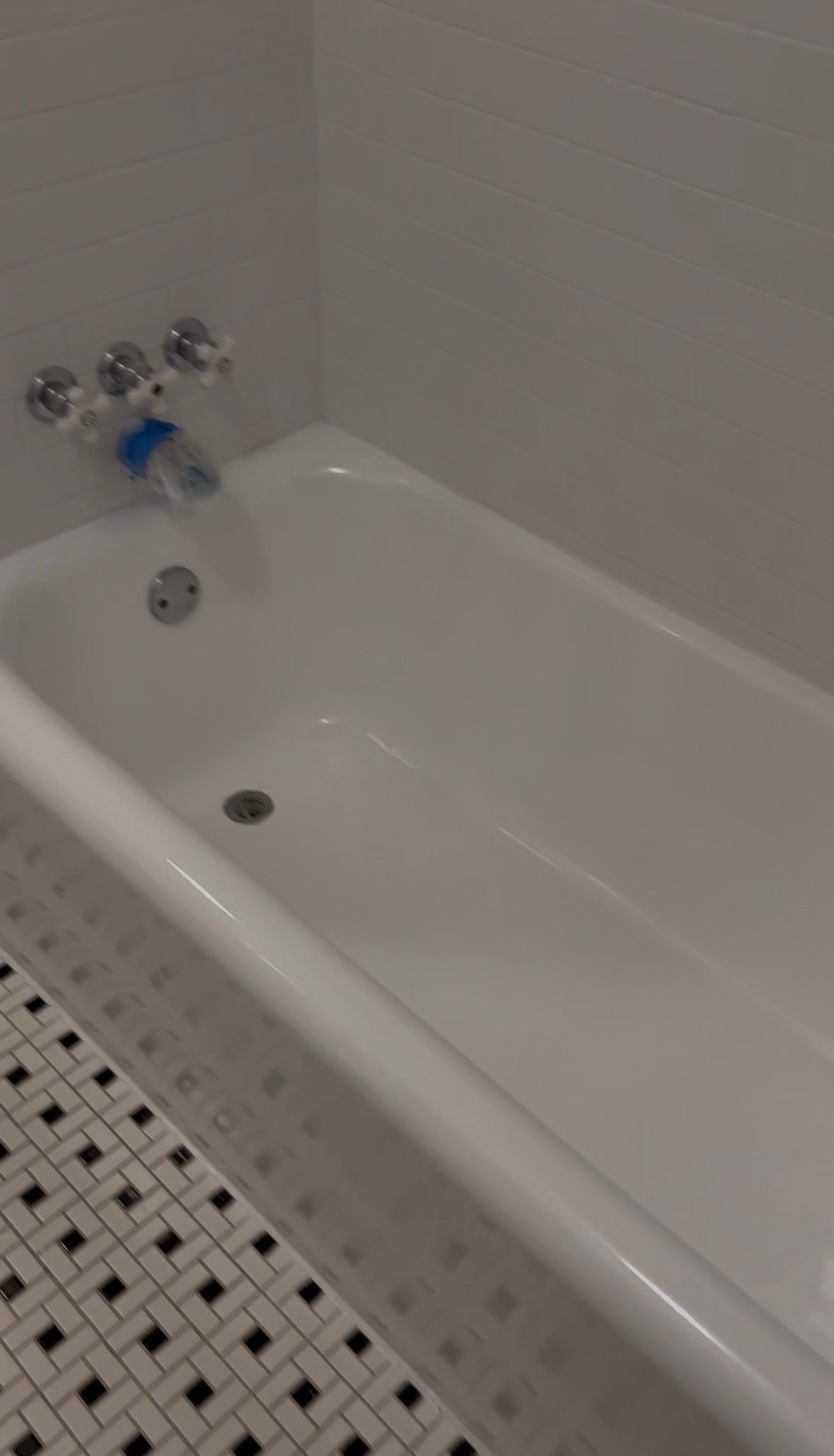 White bathtub with chrome faucet and tiled bathroom floor beside it