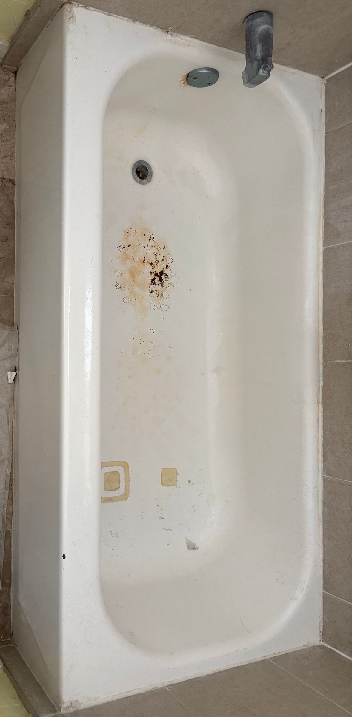 White bathtub in a tiled bathroom, with faucet and drain visible.