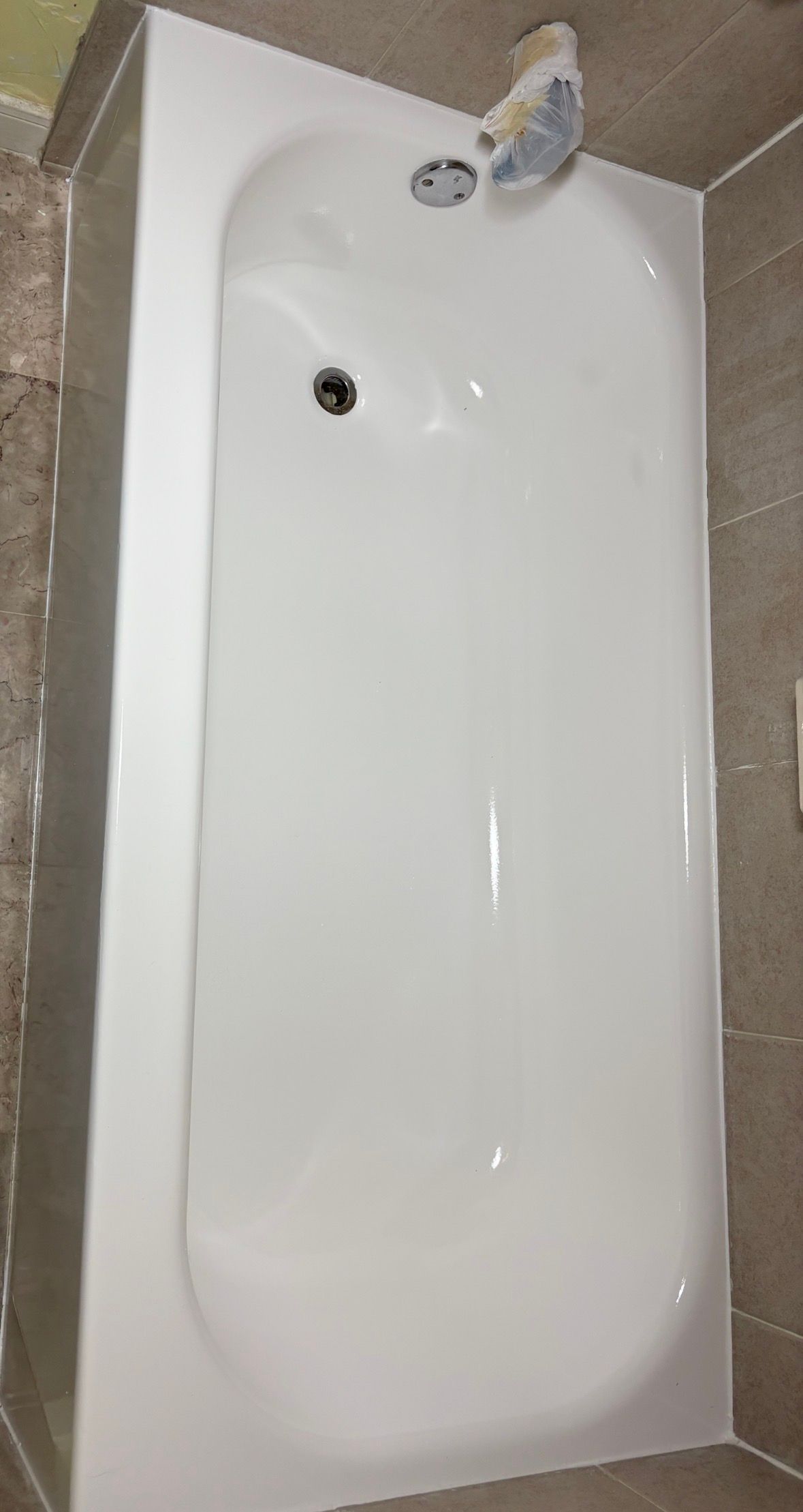 White bathtub with chrome faucet and beige tile floor, viewed from above.
