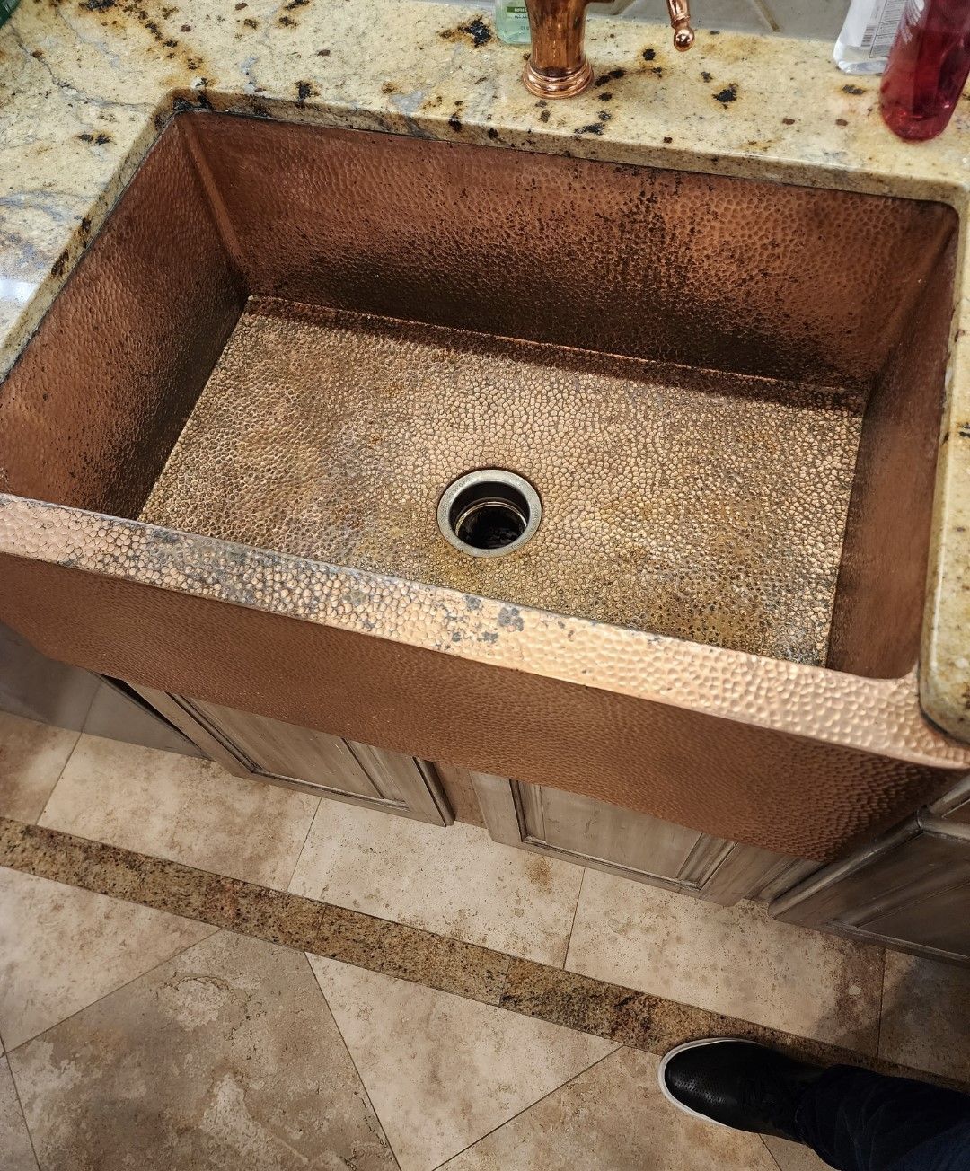 Rusty copper sink with a central drain in a tiled countertop, viewed from above.