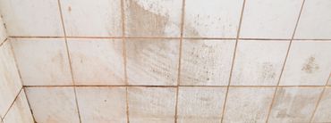 Dirty off-white tiled wall with brown stains and grime along the grout lines