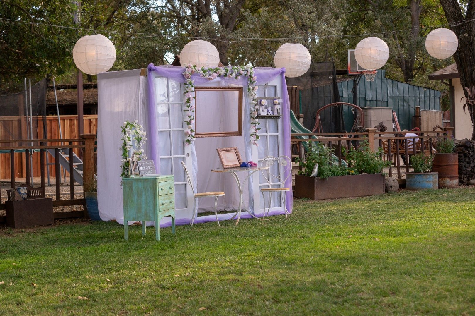 Outdoor garden photo booth setup with white lanterns and florals.