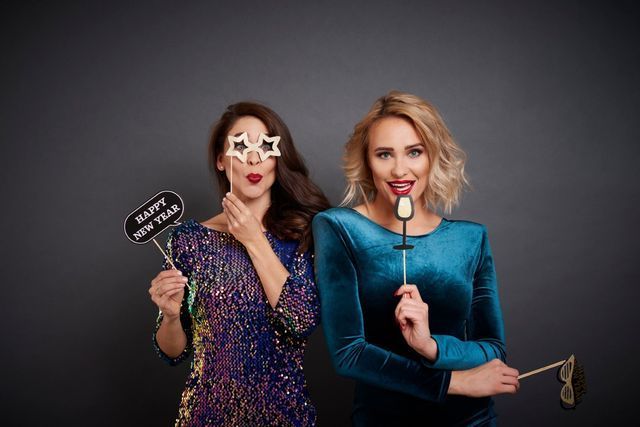 Two women in cocktail dresses with New Year's Eve photo props.