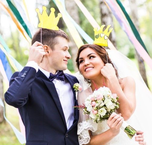 Bride and groom holding paper crown props at their wedding.