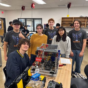 Team of students posing with a robotics competition robot in a classroom workshop