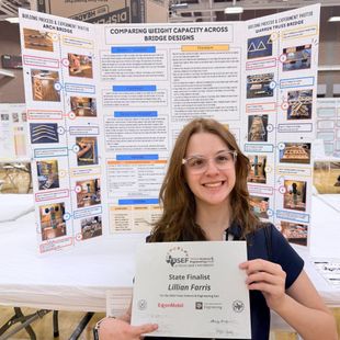 Woman smiling in front of a science poster board, holding a certificate at a research presentation