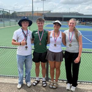 Four tennis players posing on a court, wearing medals after a match.