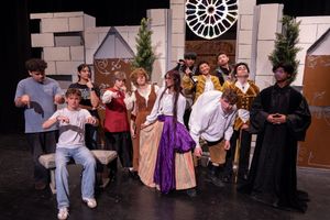 Group of people in costumes posing on a stage with castle and clock set pieces