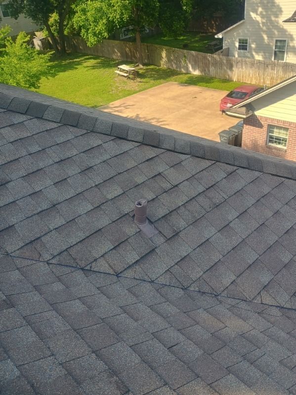 Dark gray shingled roof with a small rooftop vent, overlooking a yard and driveway beside a house