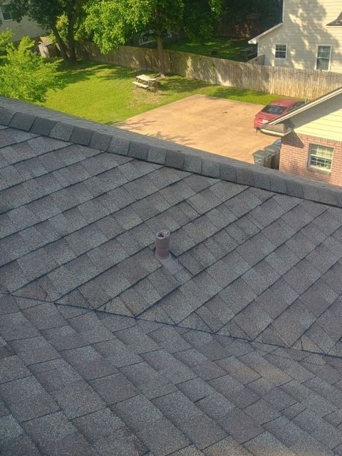 Gray shingled roof in foreground, with a driveway, lawn, and house visible beyond.