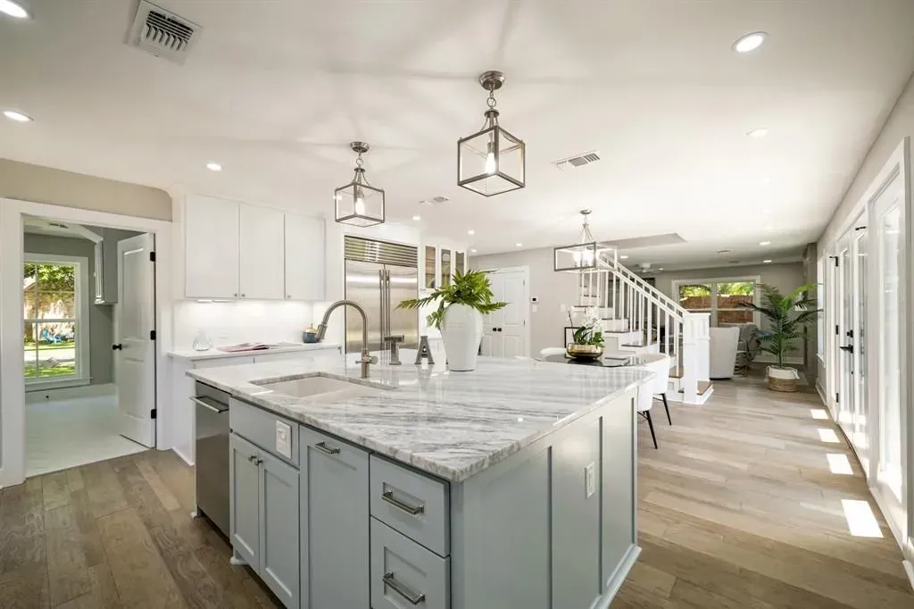 Bright modern kitchen with white marble island, gray cabinets, pendant lights, and hardwood floors