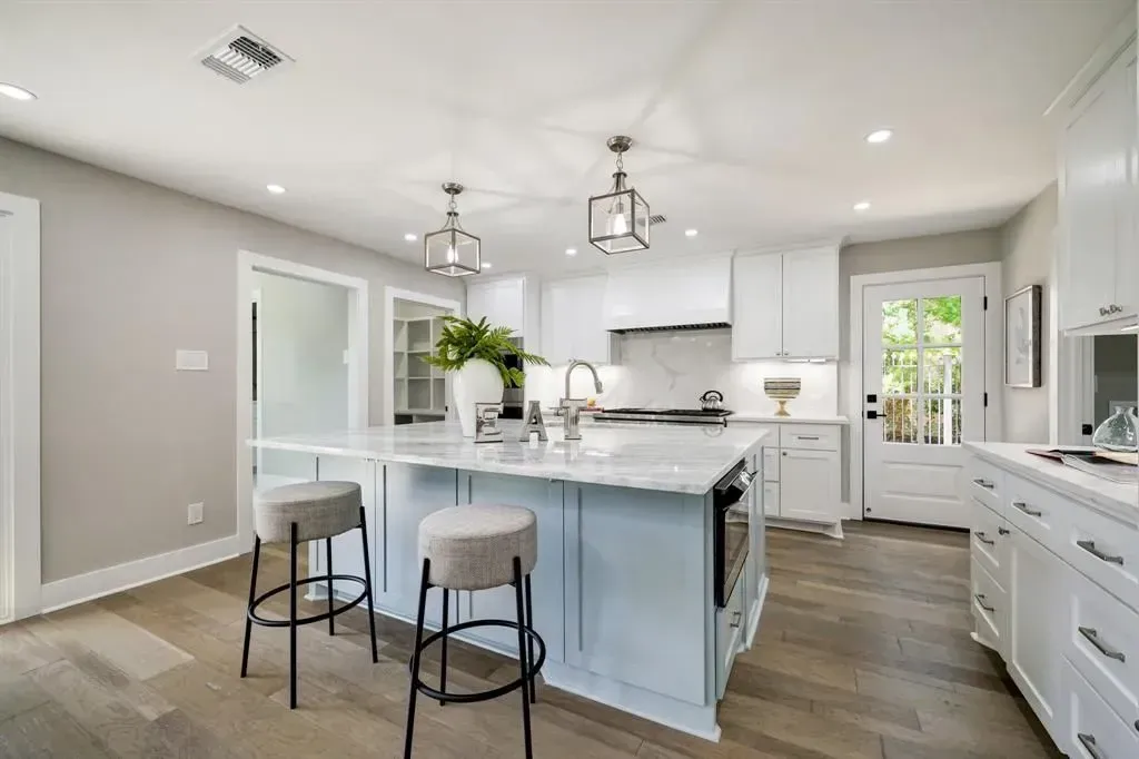 Bright modern kitchen with white cabinets, large island, and two stools in an open floor plan.