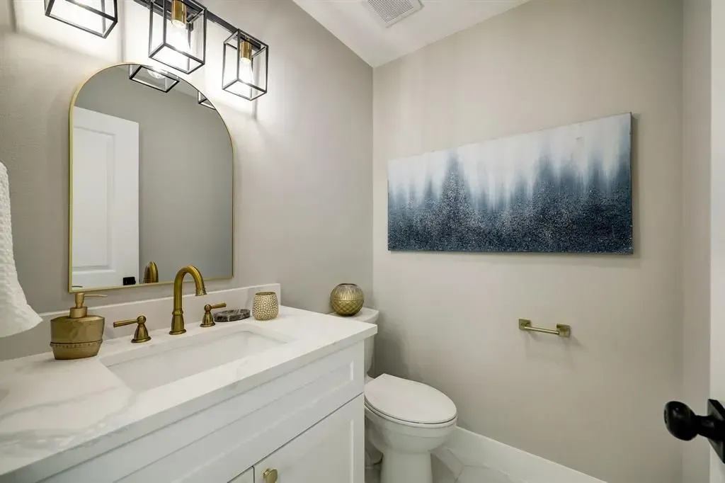 Modern bathroom with white vanity, brass fixtures, arched mirror, and blue landscape wall art