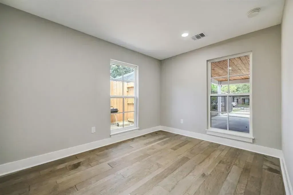 Empty room with gray walls, wood floors, and two windows letting in natural light.