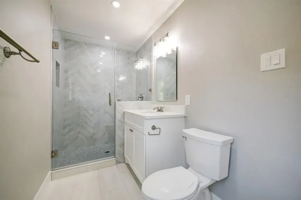 Modern gray bathroom with glass shower, white vanity, toilet, and mirror