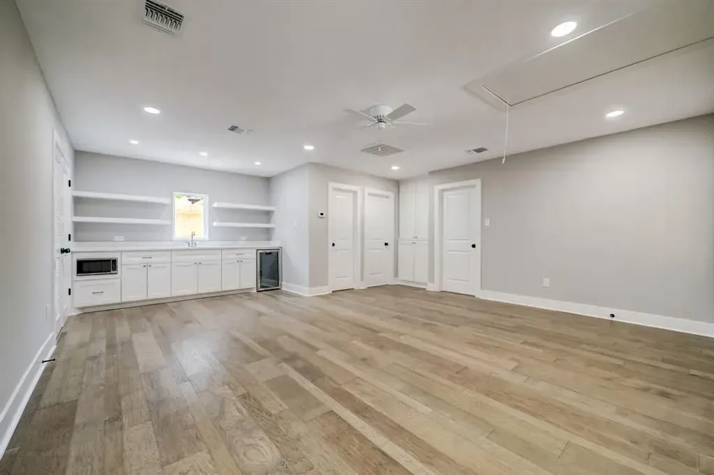 Empty modern room with light wood floors, white built-ins, and recessed ceiling lights.