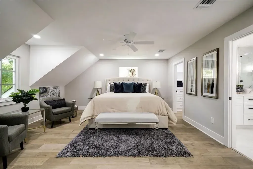 Bright bedroom with a large bed, gray chairs, wall art, and vaulted ceiling in a modern home