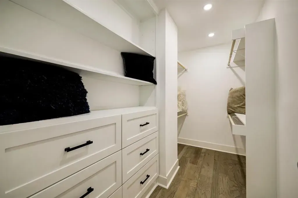 White walk-in closet with drawers, shelving, and wood floor hallway