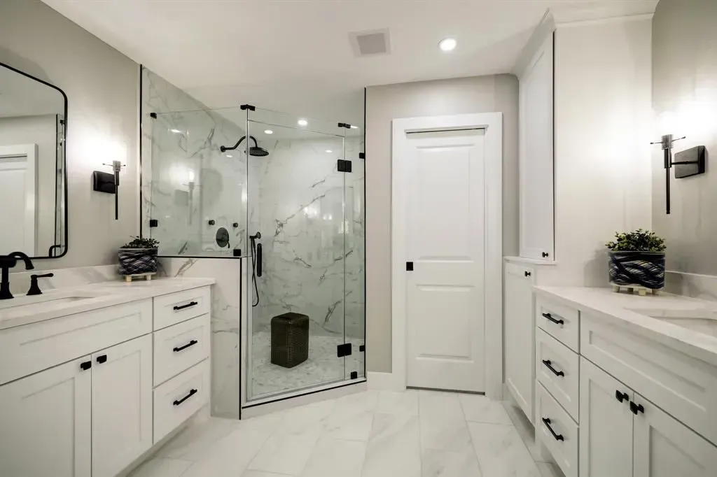 Bright white modern bathroom with double vanities, glass shower, and a centered door