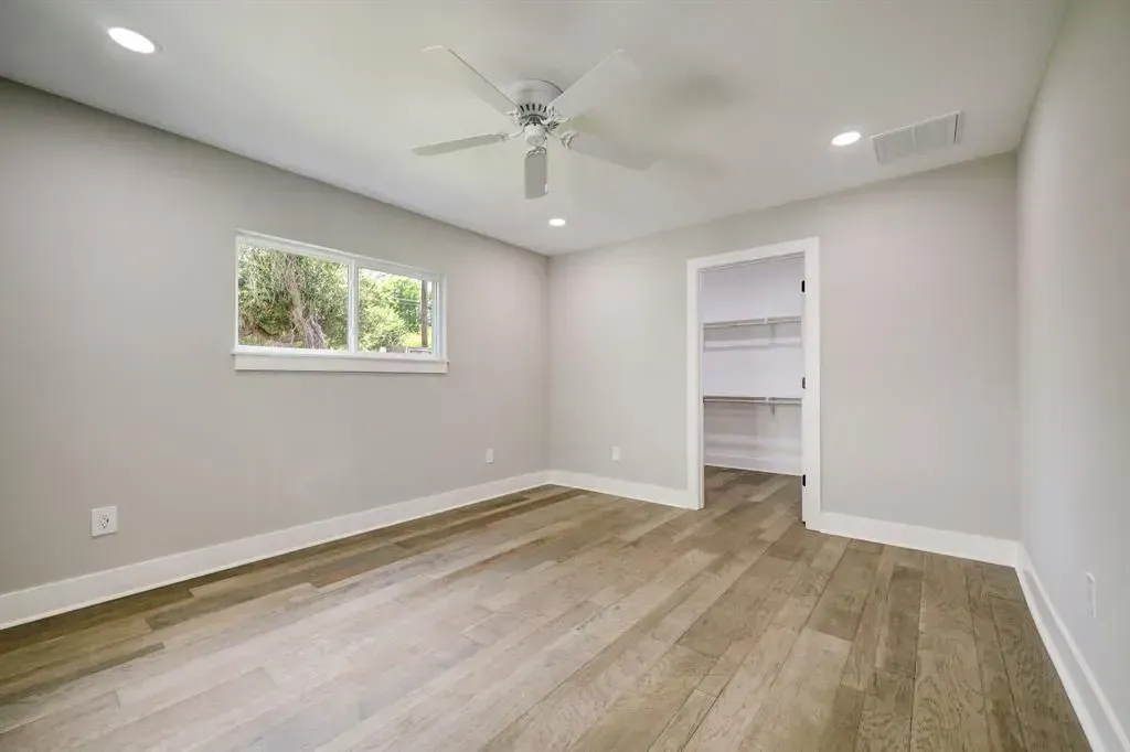 Empty bedroom with light gray walls, wood-look floor, window, ceiling fan, and open closet.