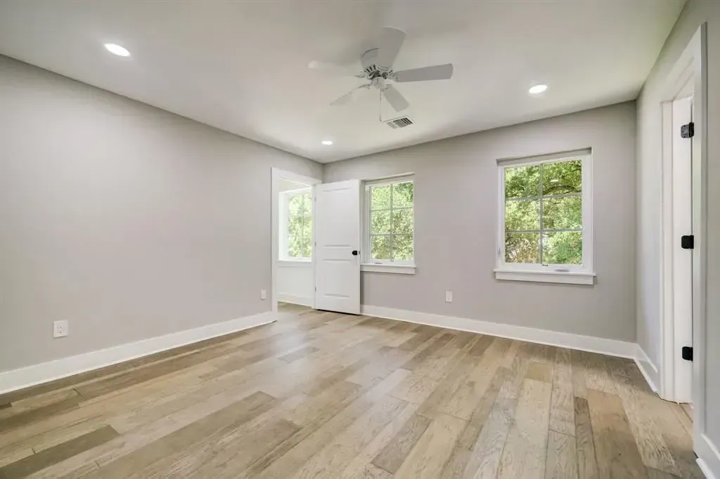 Empty modern room with light wood floors, gray walls, recessed lights, ceiling fan, and three windows